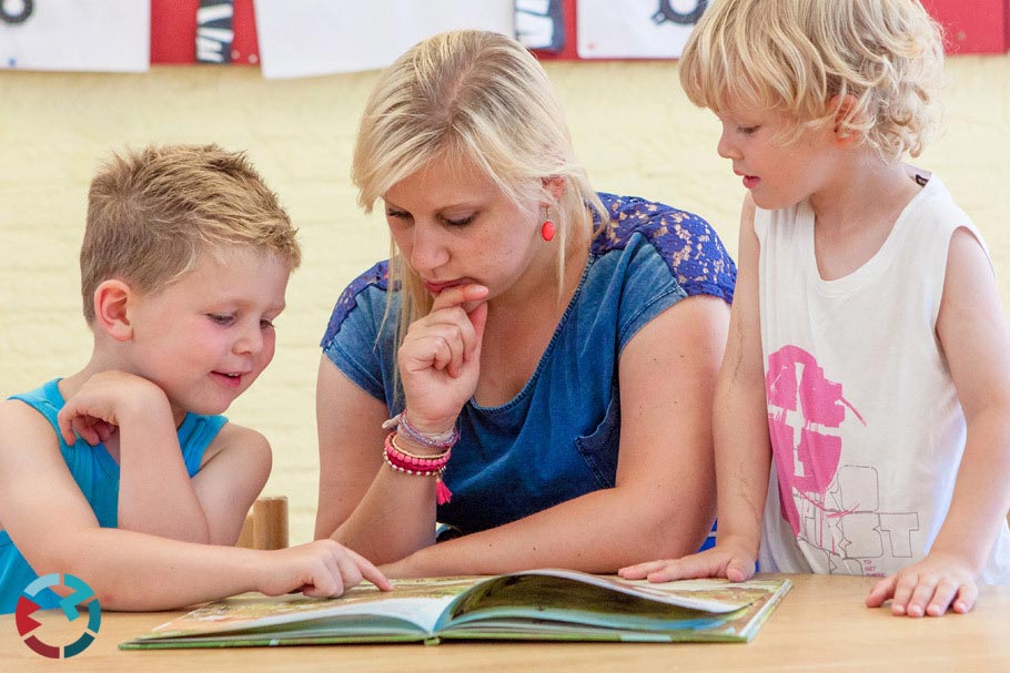 Juf leest samen met twee kinderen een boek.