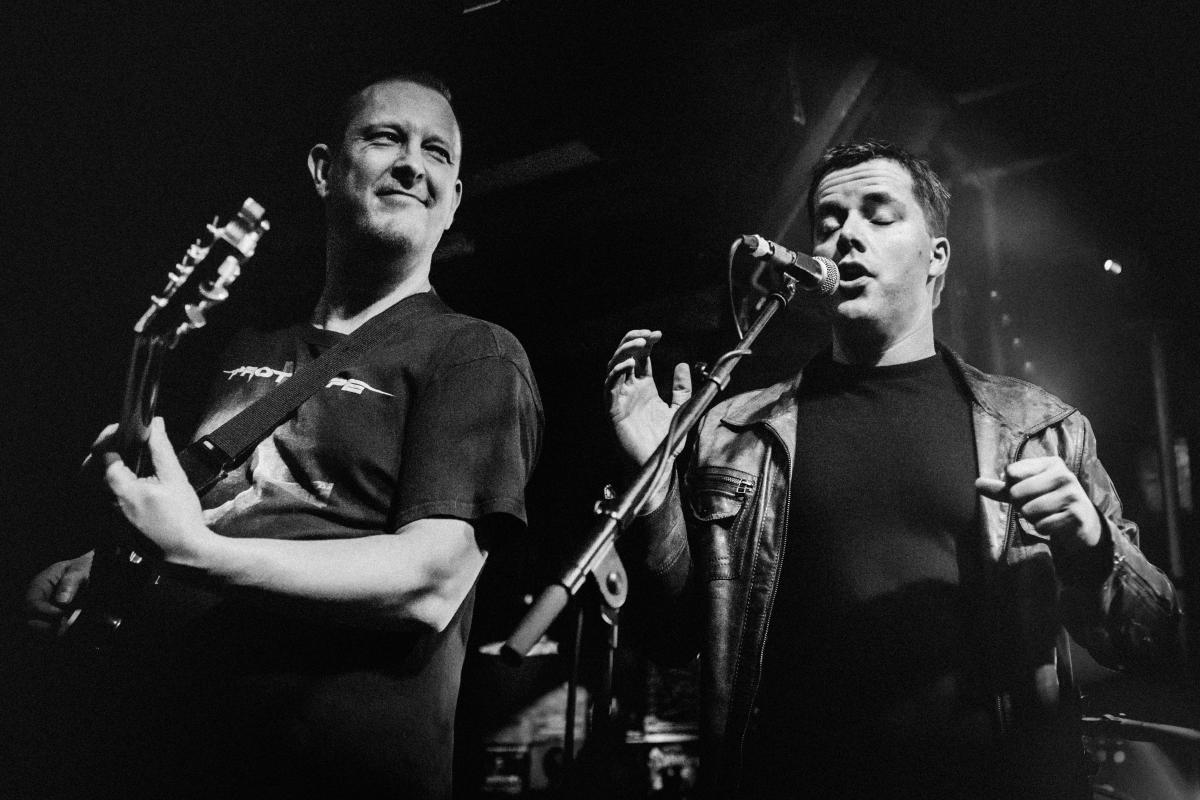 Concertfoto van gitarist met zanger.
