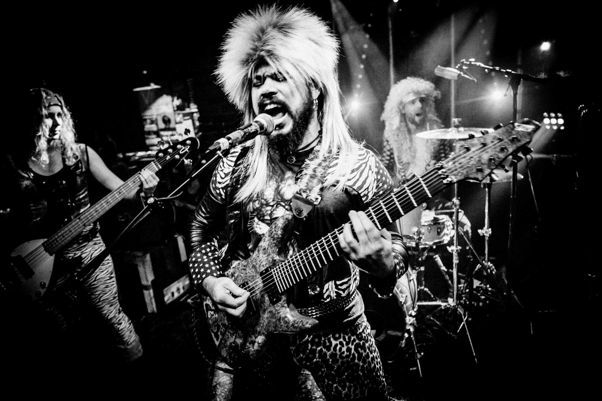 Concertfoto van gitarist met pruik op.