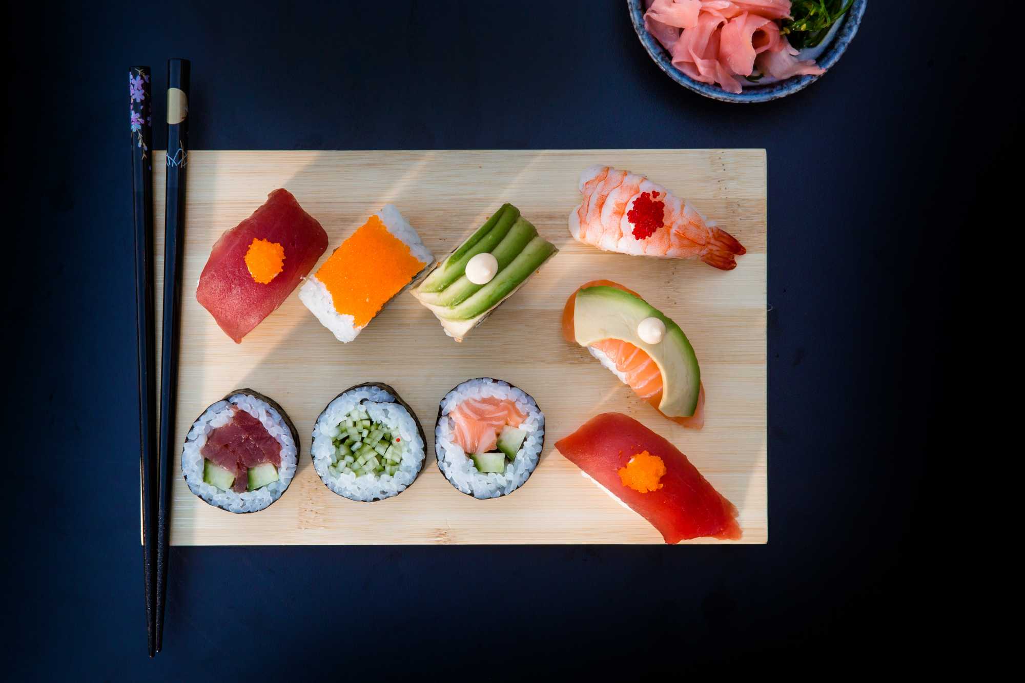 Verschillende sushi op plankje met eetstokjes er naast.