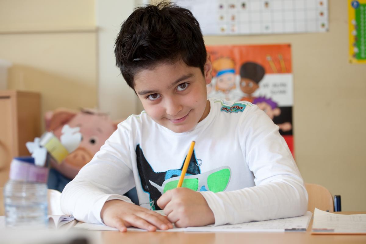 Jongen uit groep 4 kijkt op vanuit zijn werkboek