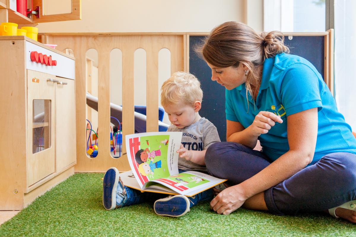 Leidster op een kinderdagverblijf leest een boek met een kleuter