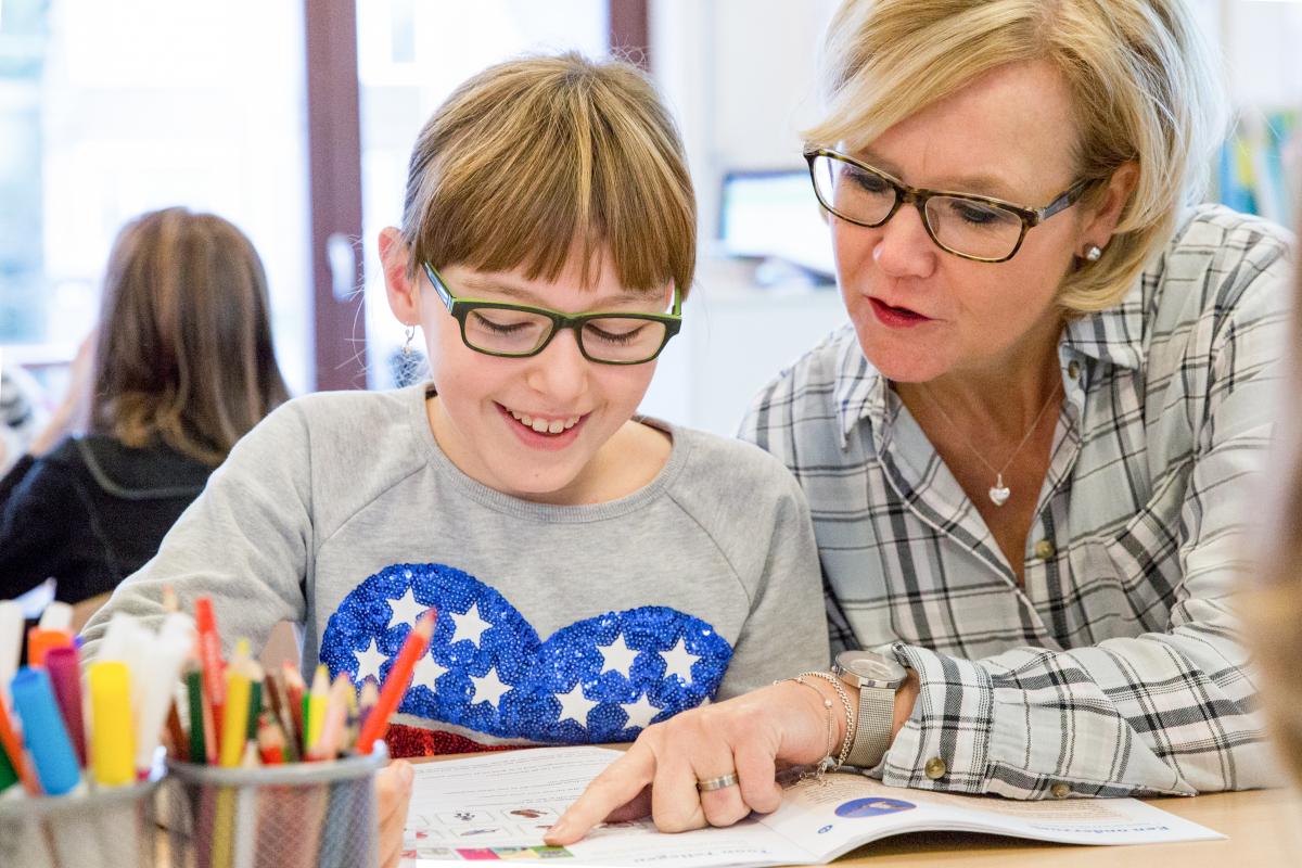 Meisje uit groep 7 krijgt uitleg over haar werkboek door haar juf.